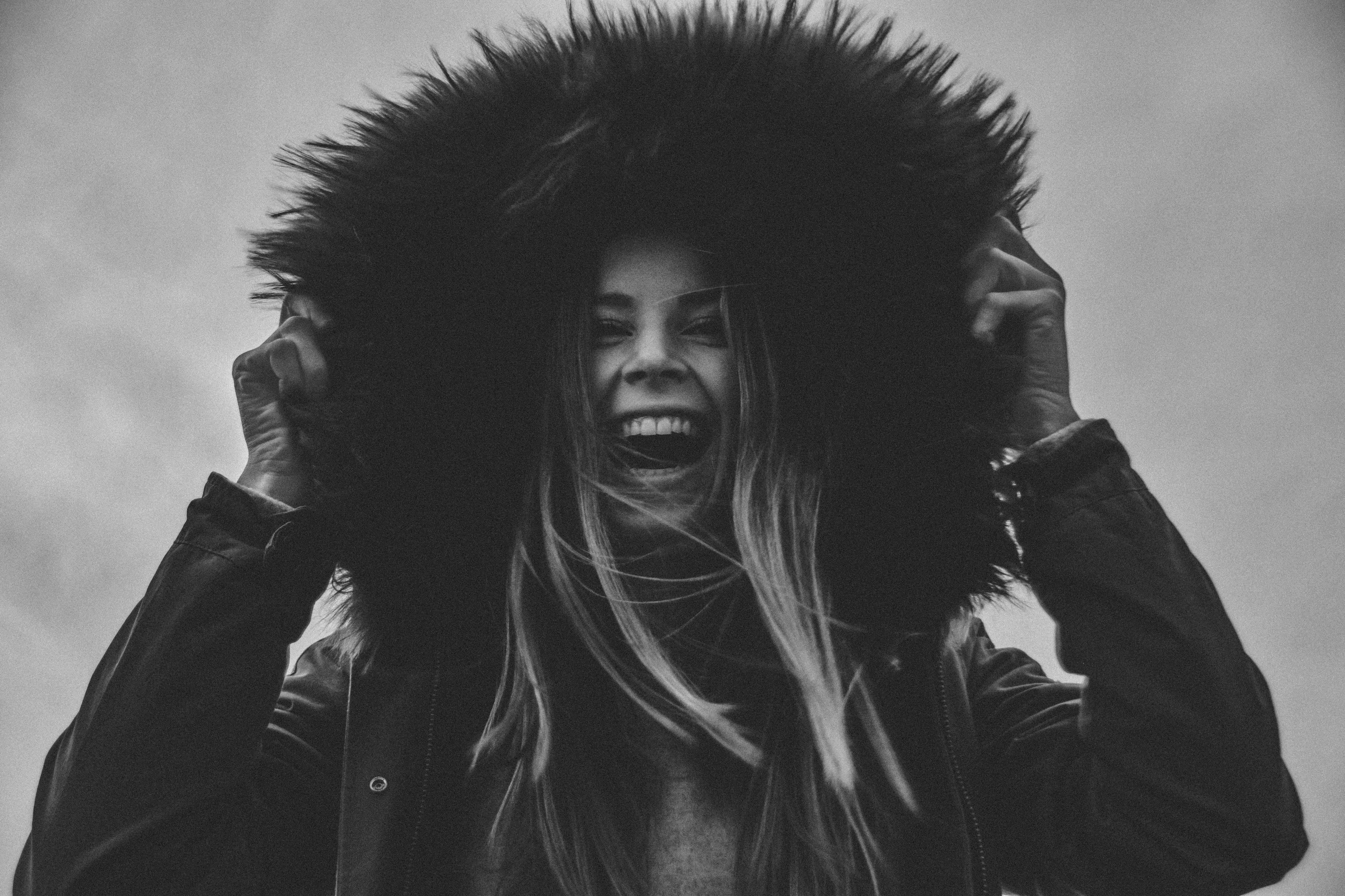 grayscale photo of laughing woman holding her hat