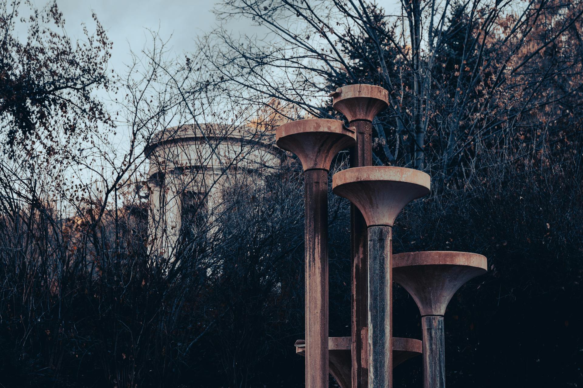 Cinematic view of rusty columns surrounded by bare trees and historical architecture.