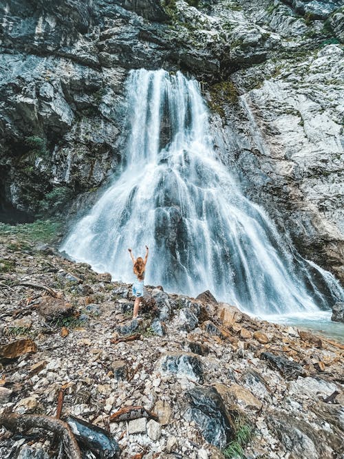 A Woman Standing Near the Waterfalls on a Rocky Mountain