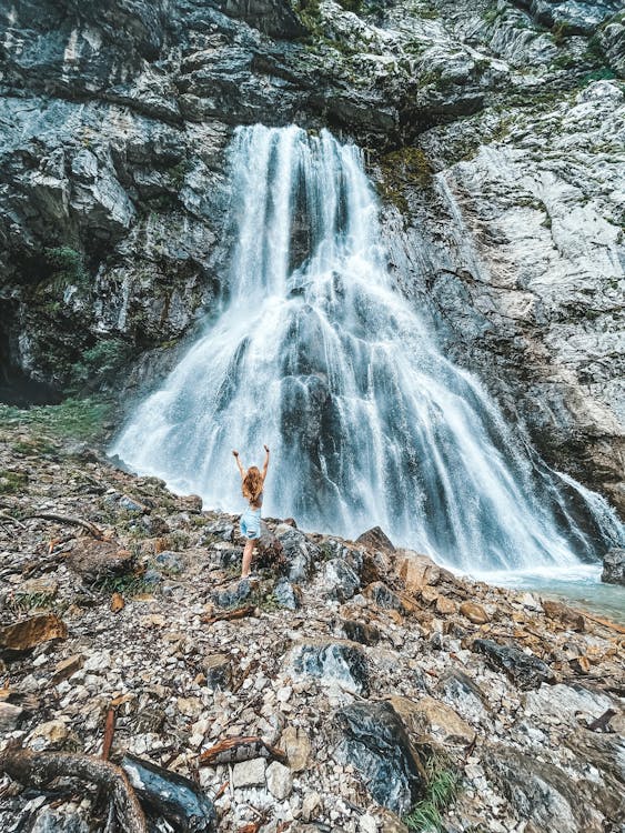 A Woman Standing Near the Waterfalls on a Rocky Mountain