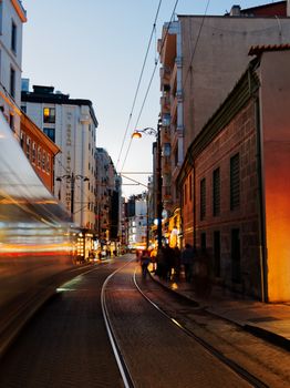 A dynamic city street view at twilight with a blurred tram passing by, creating a vibrant urban atmosphere.