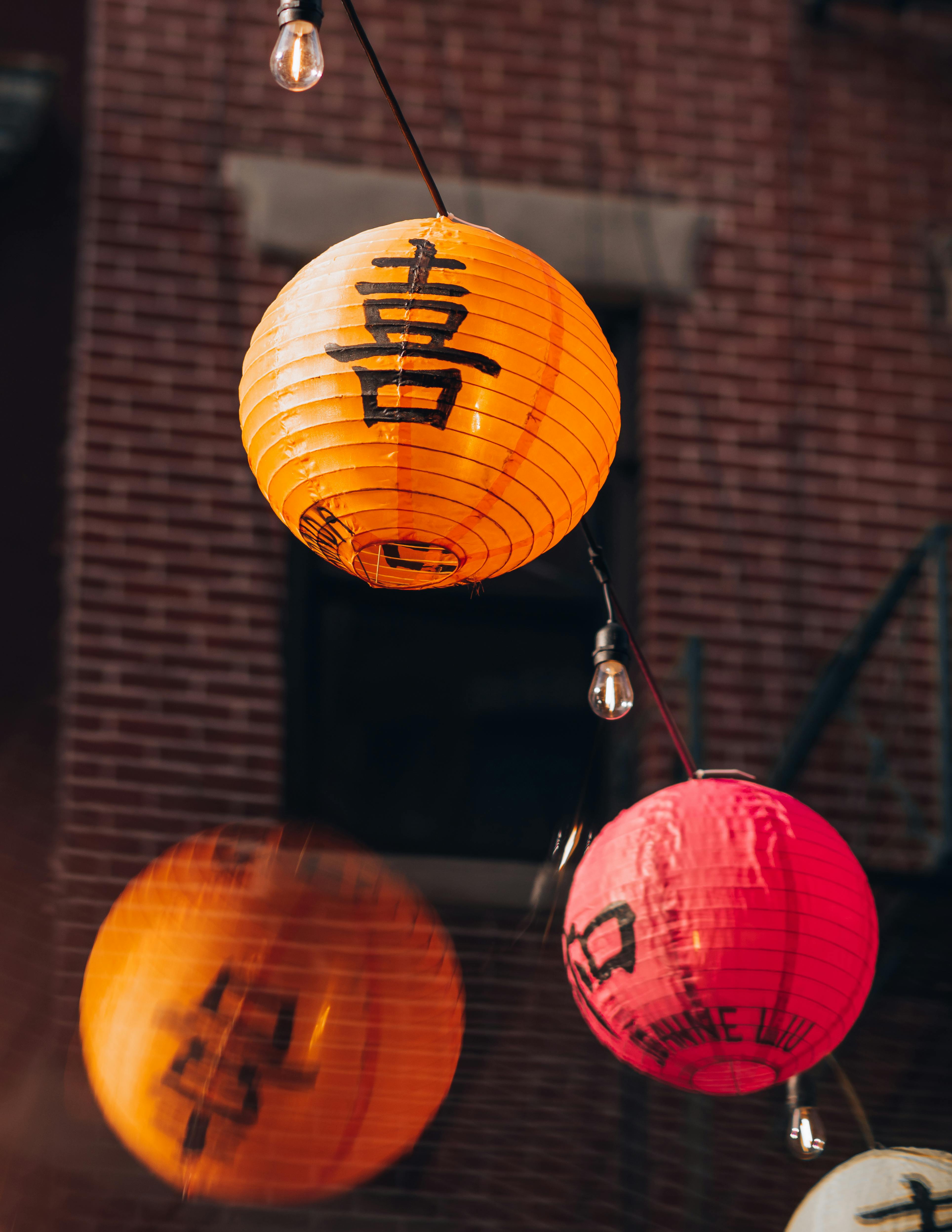 Vibrant orange and red lanterns with Chinese characters, hanging against a brick wall.