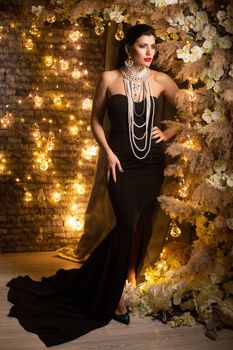 Stylish woman in black gown adorned with pearls in an elegant setting with warm lights.