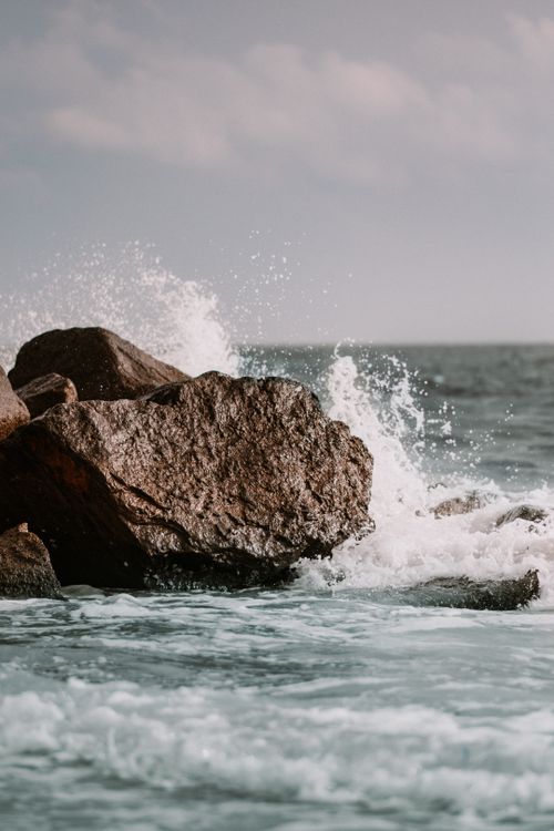 Free Dynamic ocean waves crash against rugged rocks showing nature's power and beauty. Stock Photo