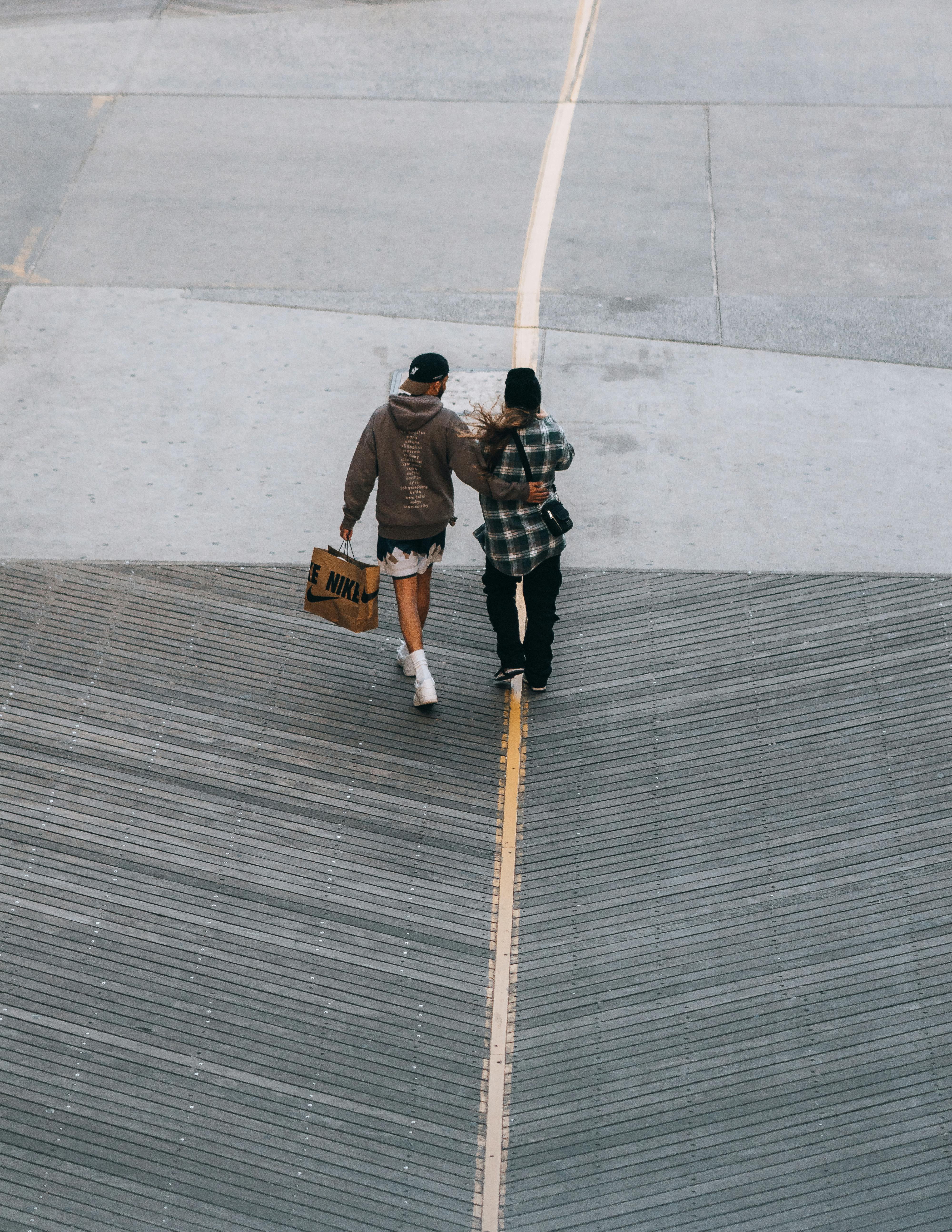 Aerial view of a couple walking together with a shopping bag on an urban concrete pathway.