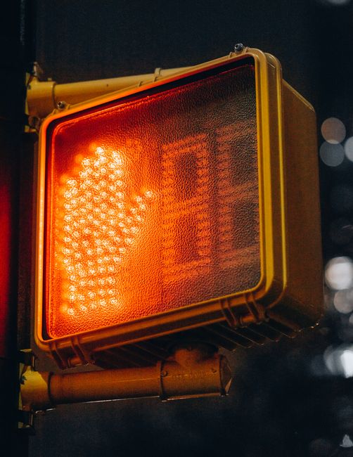 Closeup of a red hand traffic signal against a night urban backdrop, conveying an illuminated stop sign.