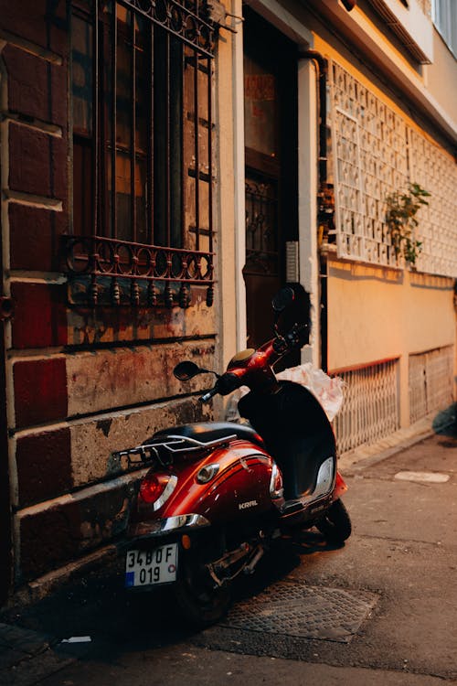 Free Red and Black Motor Scooter Parked Beside Brown Brick Building Stock Photo
