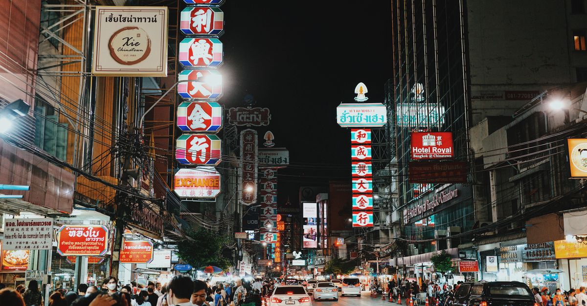 Bustling night scene in Bangkok's Chinatown with illuminated signs, people, and traffic.
