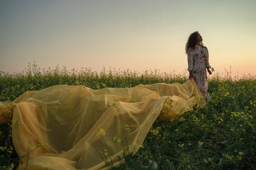 Woman Standing in Flower Field Holding Yellow Fabric