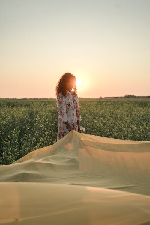 Woman Standing in Flower Field and Holding Tulle Fabric Outspread on Ground