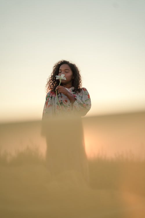 Woman Standing in Field and Smelling White Flower in Her Hand