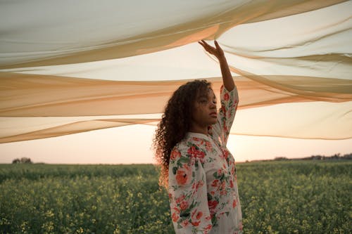 Woman Standing in Flower Field Touching See-Through Fabric