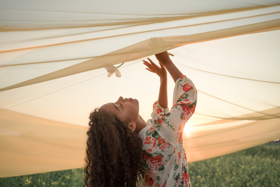 Woman with Long Wavy Hair Smelling White Flower under Transparent Fabric Outspread Above