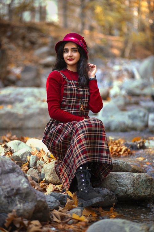 Free Woman in a plaid dress sitting by the river in Tehran, surrounded by autumn leaves. Stock Photo