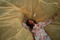 Young Woman Laying on Yellow Tulle Outspread on Meadow
