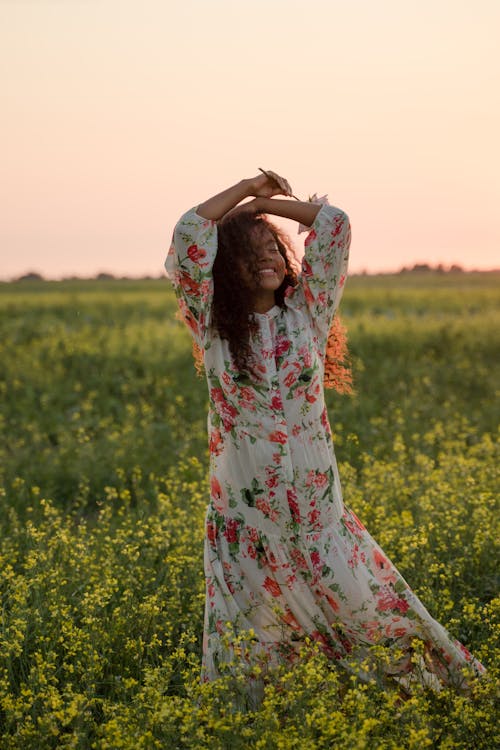 Young Woman with Raised Arms Standing in Flower Field and Smiling