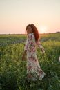 Cheerful Woman in Floral Summer Dress Dancing in Flowery Meadow at Sunset