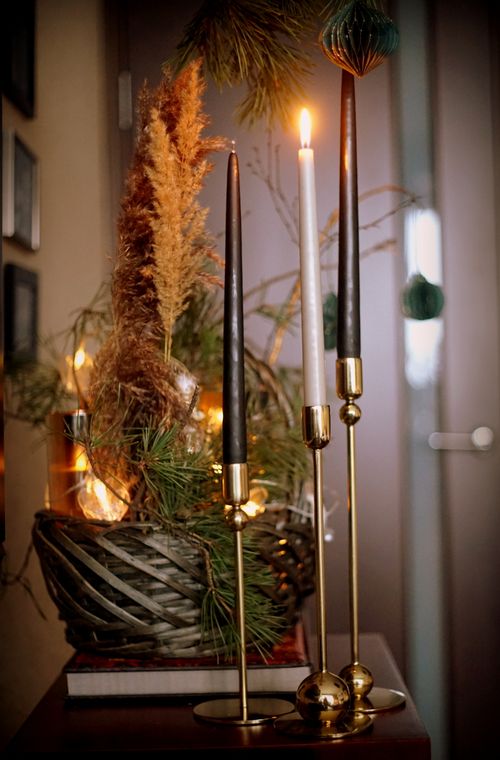 Free A cozy indoor display featuring tall candles on brass holders with a wicker basket filled with pine and twigs. Stock Photo