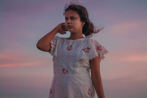 Free A young woman in a floral dress stands against a beautiful sunset, creating a serene and contemplative scene. Stock Photo