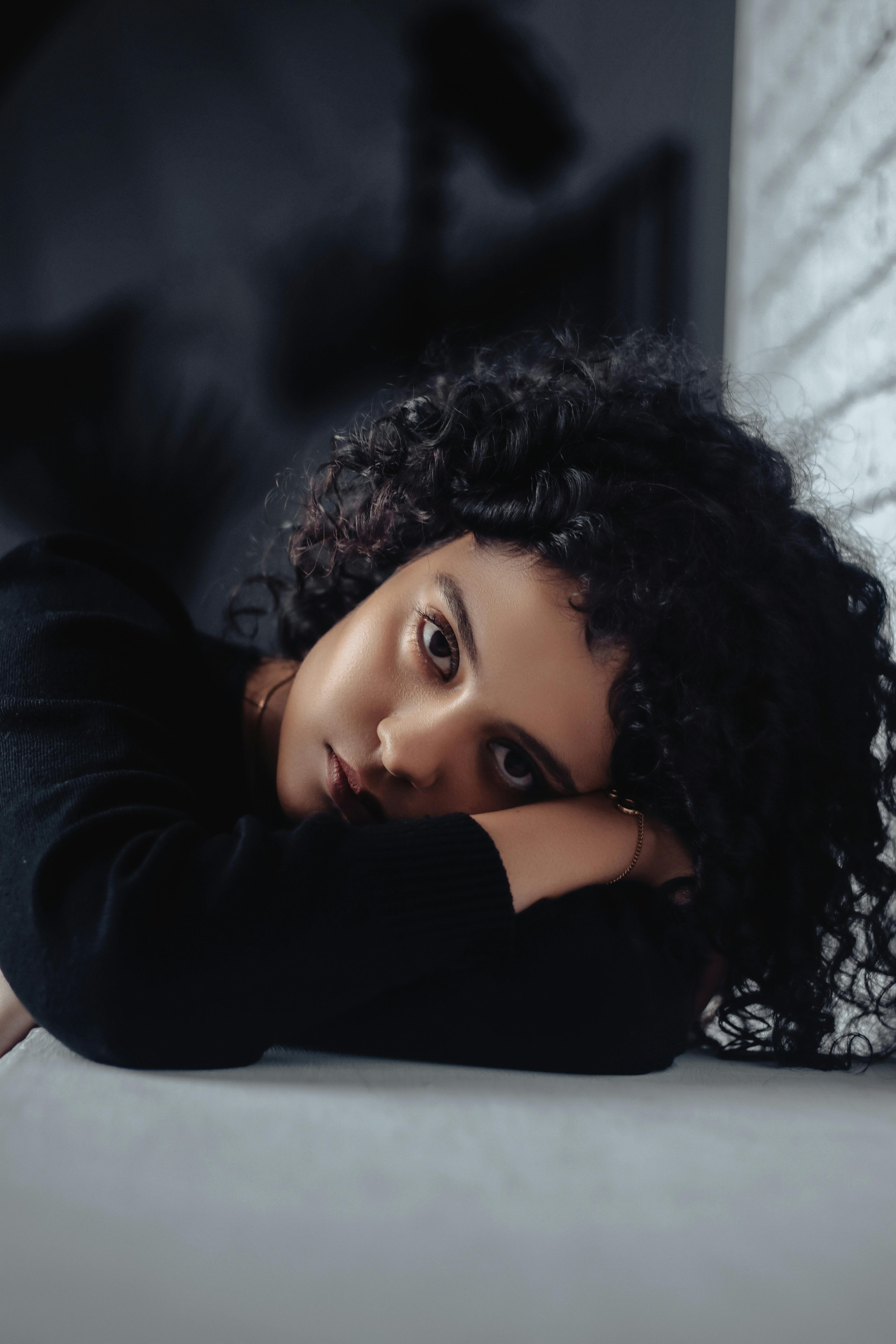 A woman with curly hair lying on a white surface, wearing a black long-sleeved top in Ukraine.