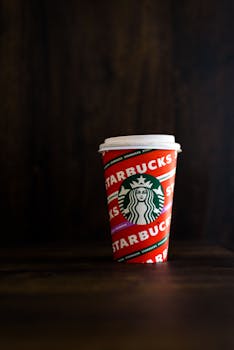 Vertical shot of a colorful Starbucks cup placed on a wooden table with a dark background, creating a moody atmosphere.