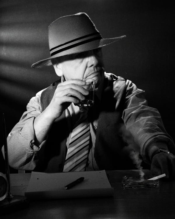 Grayscale Photo of a Man with a Hat Holding a Glass