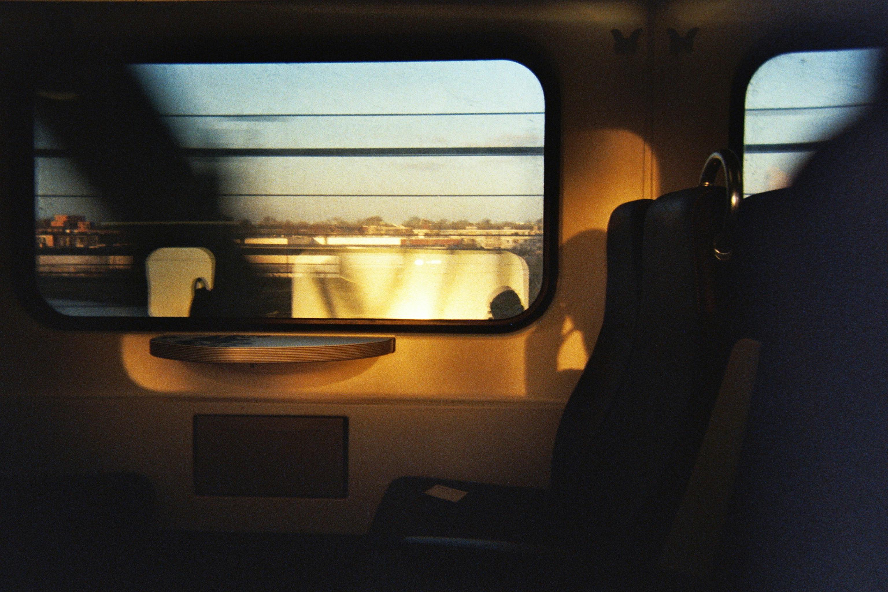 Sunlight streams through a moving train's window, illuminating its interior seats.
