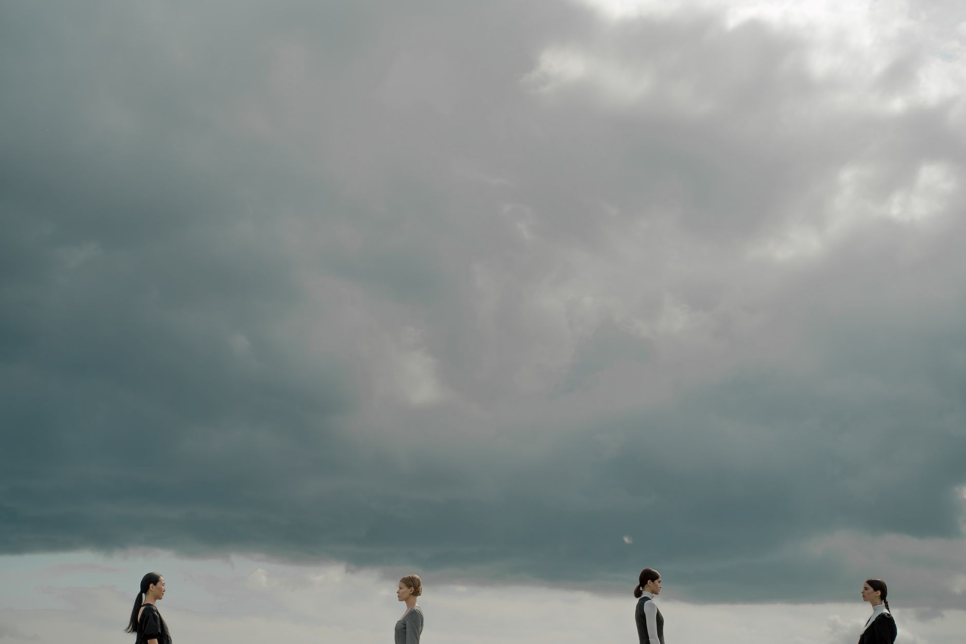 Four people beneath dramatic cloudy skies, evoking modern social themes.