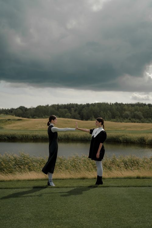 Free Two women maintain social distance in a grassy field under a cloudy sky. Stock Photo