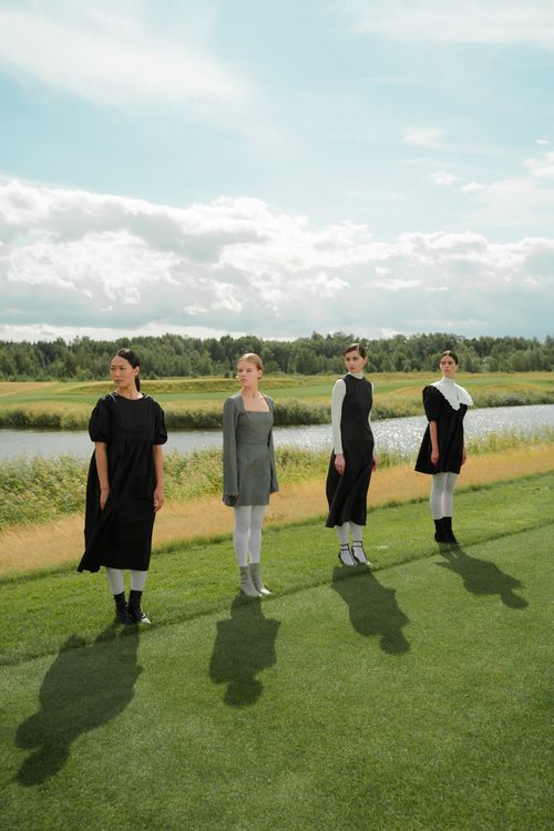 Free Four women in black and grey dresses standing on grassy field by a river under blue sky. Stock Photo