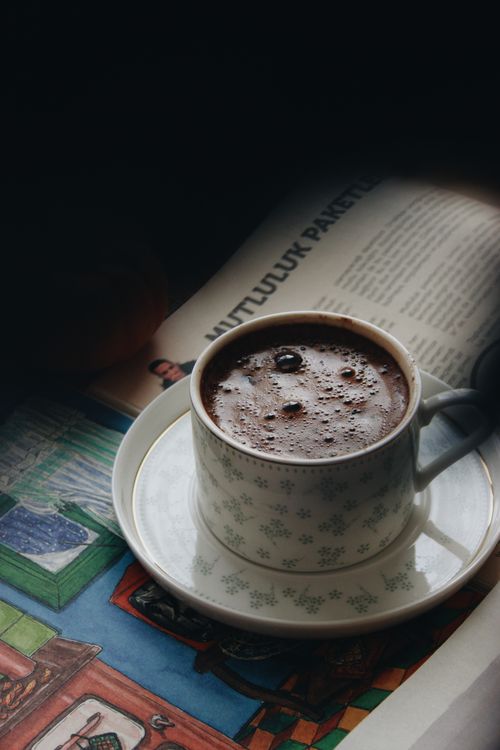 Free Warm cup of hot chocolate on a saucer beside a newspaper, perfect for a cozy indoor moment. Stock Photo