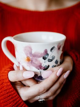 Woman in red sweater holding floral patterned cup, enjoying a cozy hot drink moment.. woman, sweater, holding