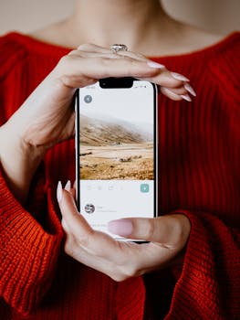 A woman in a red sweater holds a smartphone displaying a scenic landscape image.