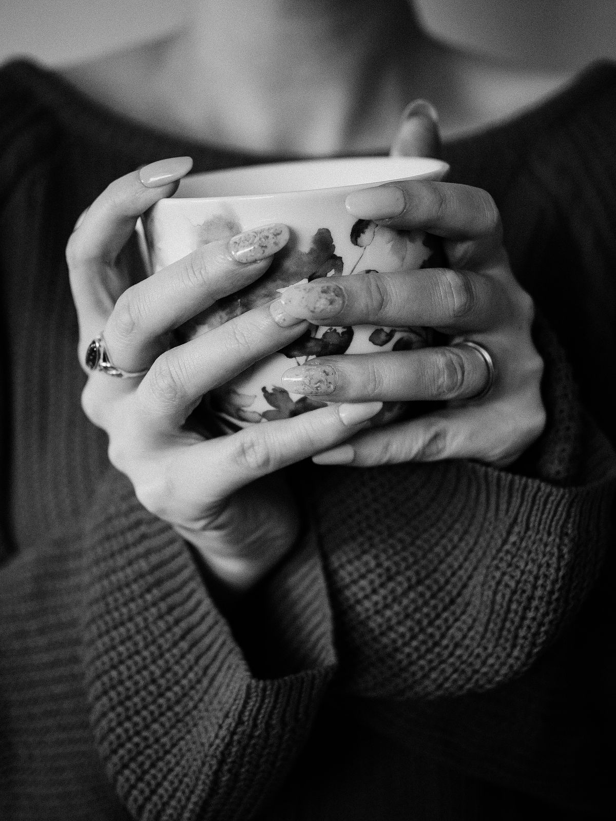 A woman holds a floral mug in a cozy black and white setting, exuding warmth and comfort.