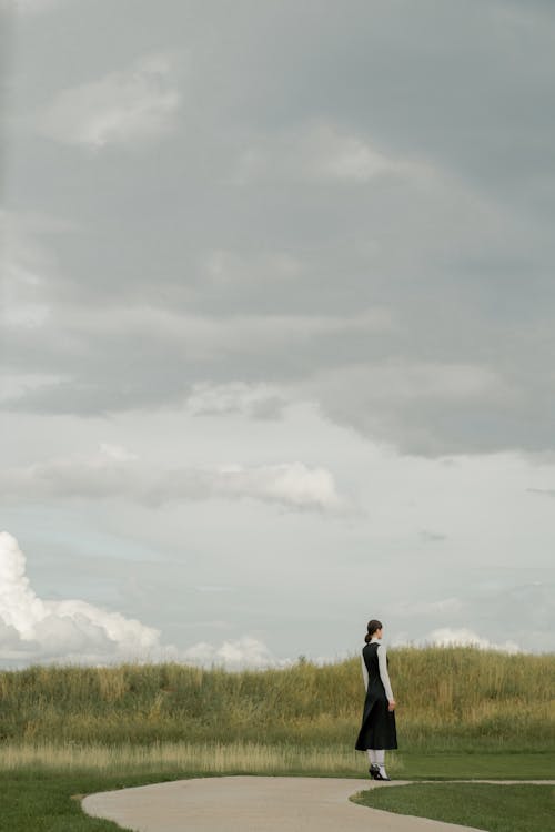 Free Photo of a Woman Standing on a Path Under White Clouds Stock Photo