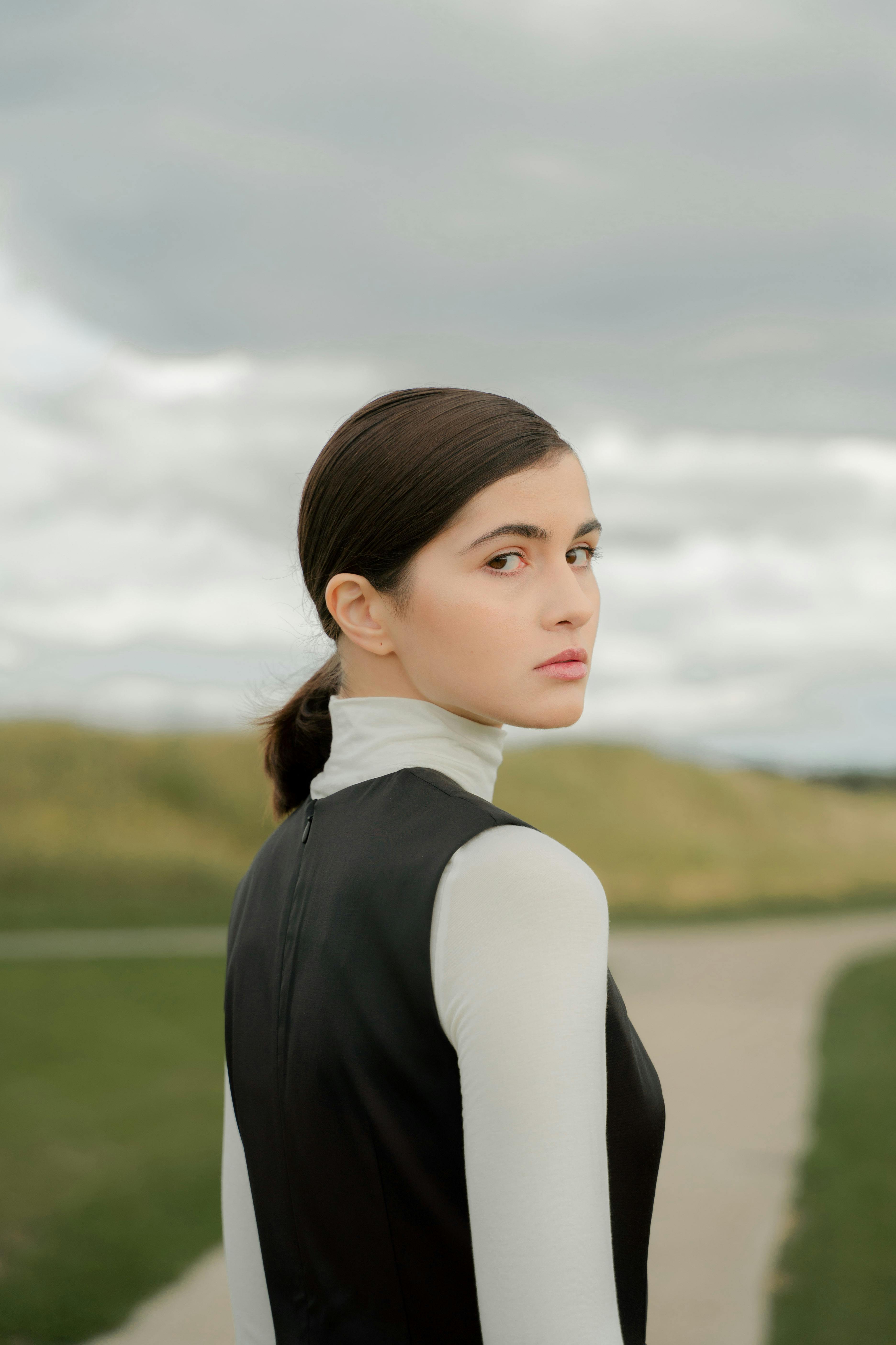 Sophisticated portrait of a woman glancing back outdoors on a cloudy day.