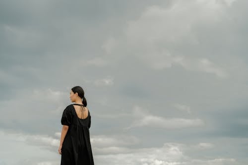 Back View of a Woman Standing Under White Clouds