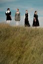 四个穿着简单连衣裙的女人站在蓝天下的草小山上
