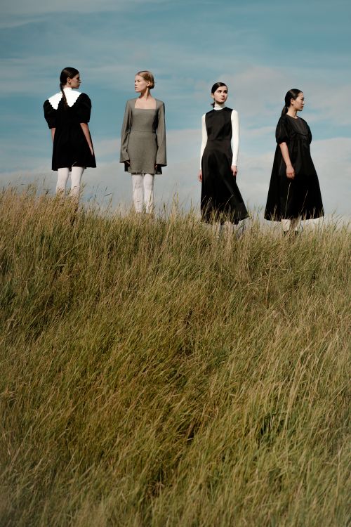 Free Four women in simple dresses standing on a grassy hill under a blue sky. Stock Photo