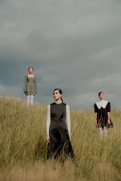 Free Three women pose stylishly in a lush grass field under an overcast sky. Stock Photo