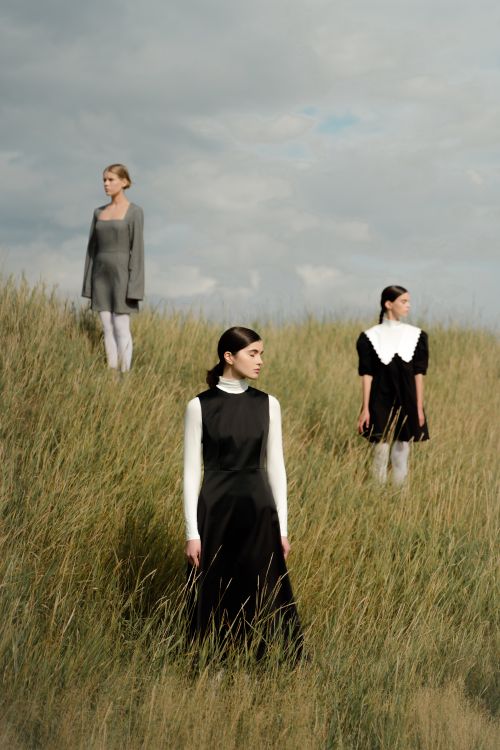 Free Three women in vintage dresses stand in a rural meadow on a cloudy day. Stock Photo