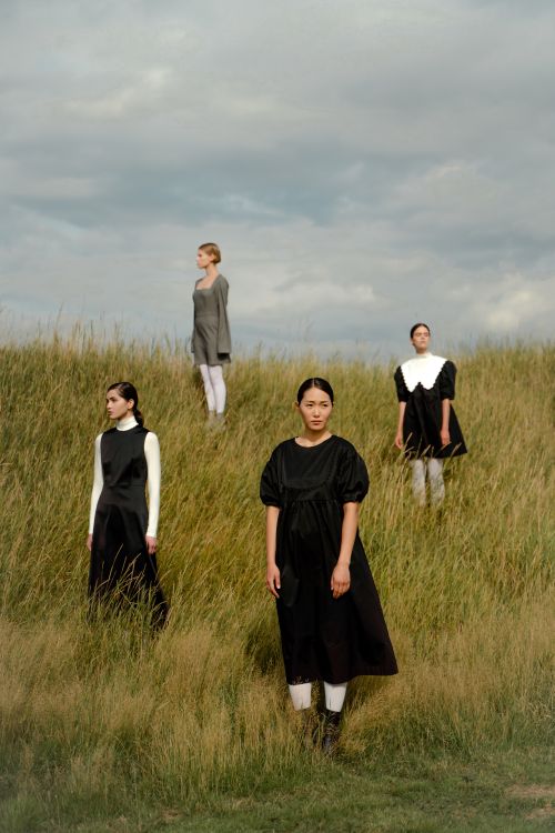Free Models in stylish dresses stand in a scenic grassy field under a cloudy sky. Stock Photo