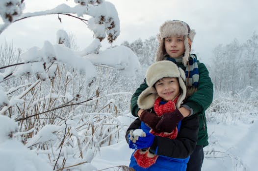 Two boys in winter attire embracing amid a snowy landscape, exuding warmth and joy.
