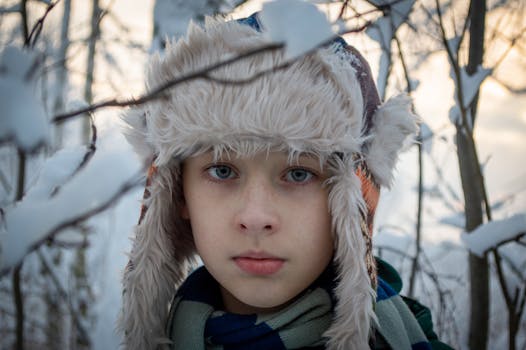 Close-up portrait of a young boy in a trapper hat surrounded by winter snow.