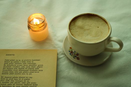 A cozy setting with a cup of coffee, candle, and open poetry book on a table.