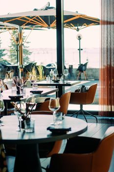 Elegant restaurant interior with modern design, featuring sea view through large windows, empty tables set for dining.