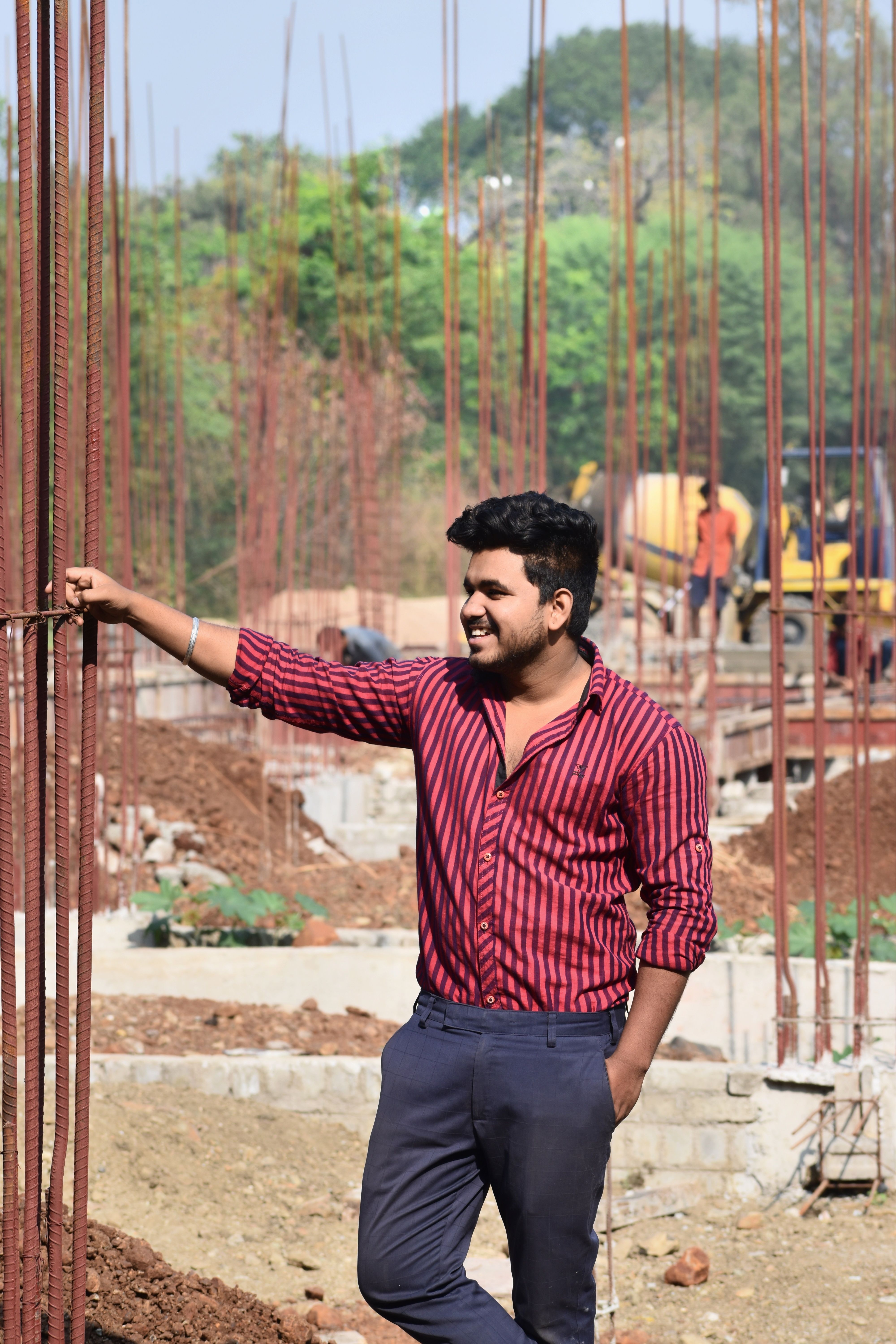 Smiling man at a construction site holding rebars, showcasing construction progress.