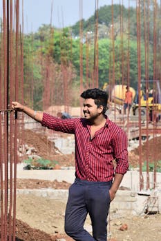 Smiling man at a construction site holding rebars, showcasing construction progress.