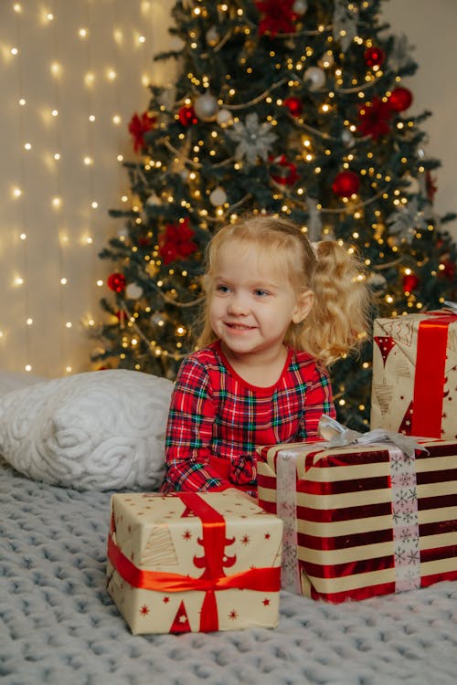 Little Girl in Red and Green Plaid Dress Sitting on Bed with Gifts