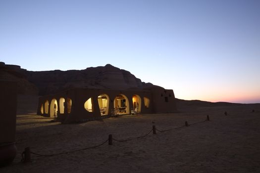 A serene desert gazebo illuminated from within at twilight, surrounded by vast sandscape.